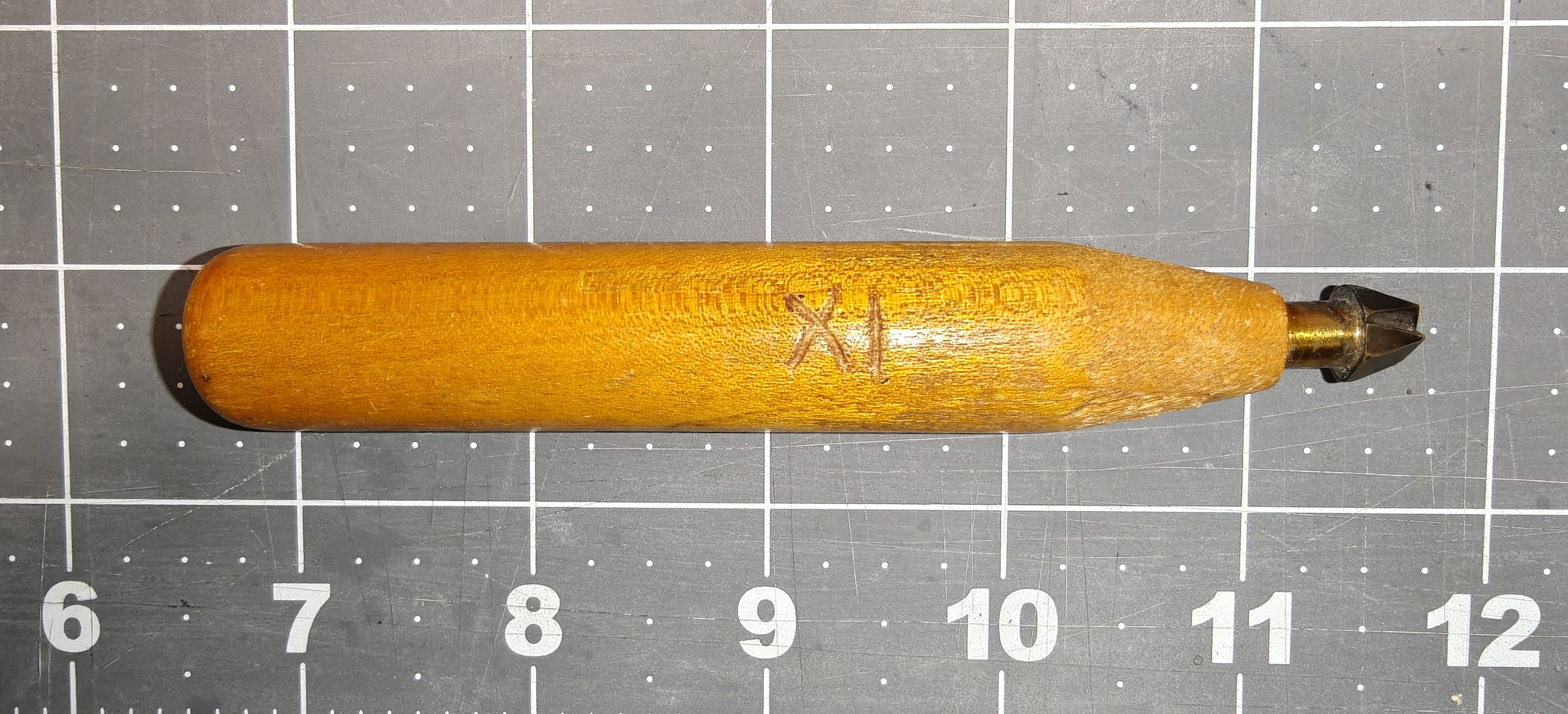 Professional stamp No. IX: a turned wooden handle with its number cut into the wood, and a brass die, on a cutting mat ruled in inches. The whole stamp is a little under six inches long.