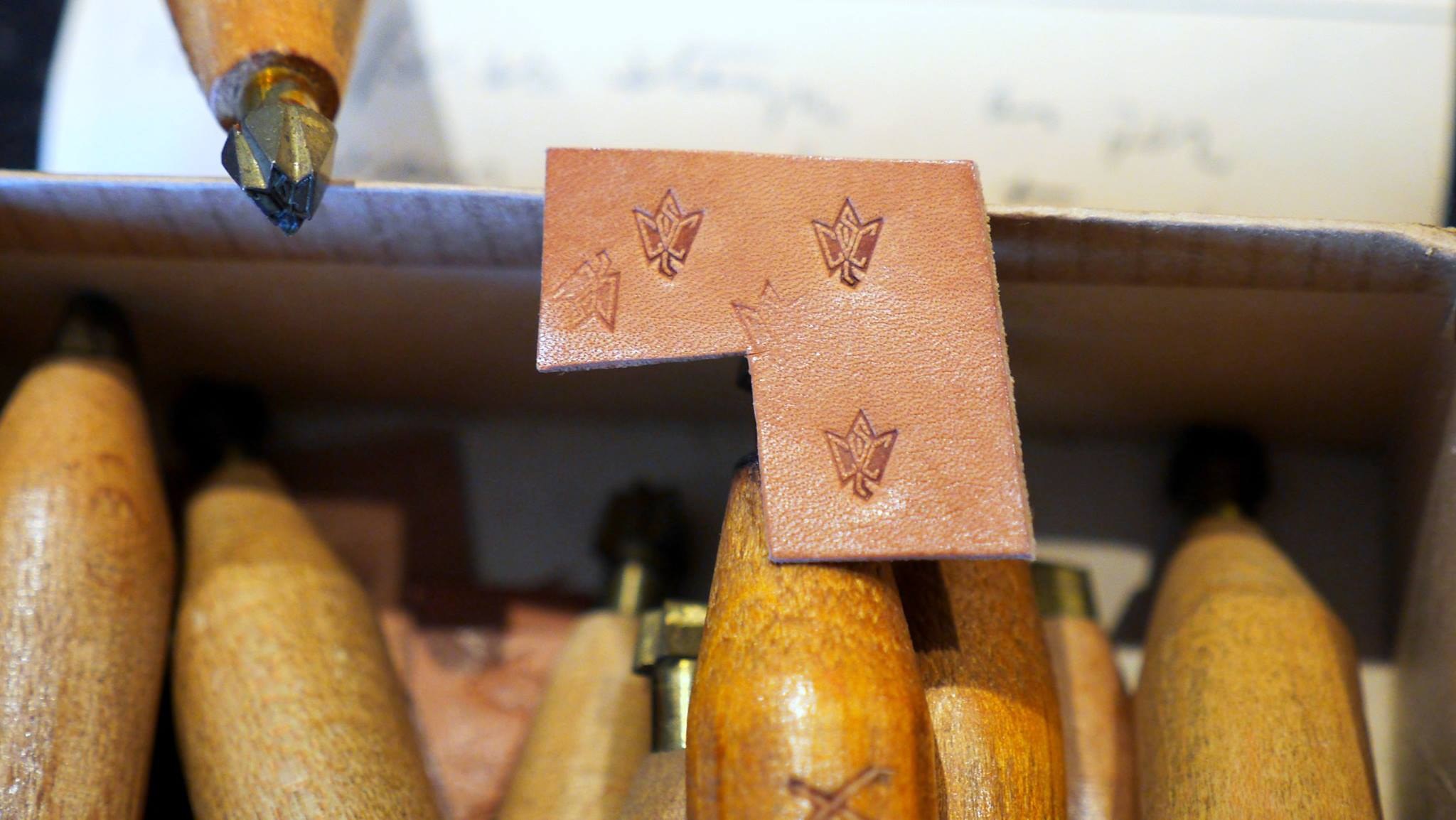 A small piece of tan leather struck four times with the monogram, held above a box of stamps with turned wooden handles.