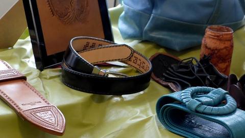 Leatherwork on a green tablecloth: a black belt, a tooled sheath, a teal braided belt and a carved box
