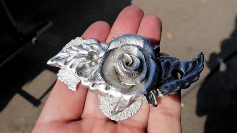 A finished pewter casting: a rose with leaves, held in the hand