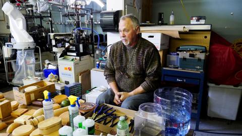 A workshop leader sits behind a table of wooden box forms, glue bottles and tools in a workshop
