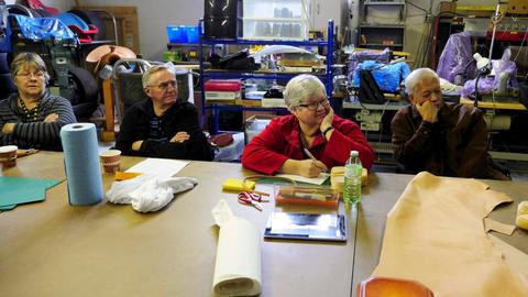 Members sit at a long table with leather sheets and paper towels at a lasting boxes workshop