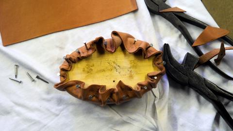 Leather tacked and gathered around an oval form next to lasting pliers and loose tacks