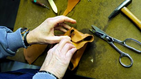 Hands fold damp tan leather around a block form beside scissors and a hammer