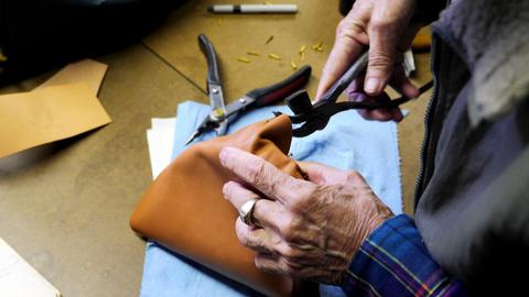 A member pulls tan leather over a box form with lasting pliers on a blue cloth