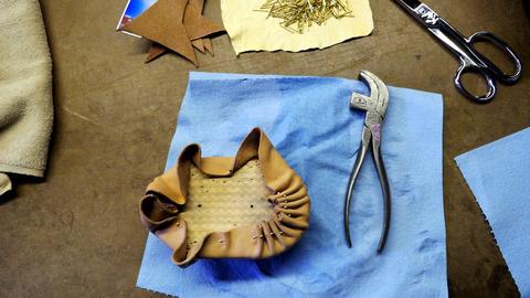 Leather tacked around a box form on a blue cloth, with lasting pliers and scissors nearby