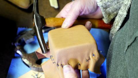 A member taps tacks into damp leather stretched over a square box form with a hammer