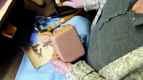 Leather being stretched and tacked around a square wooden form on a blue cloth