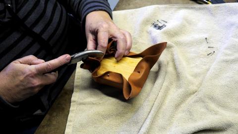 Lasting pliers pull brown leather taut around a box form on a towel