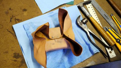 Wet leather stretched around a form for a lasted box, next to lasting pliers, a hammer and knives