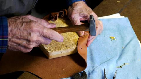 A hammer drives tacks into leather lasted over a wooden form on a blue cloth