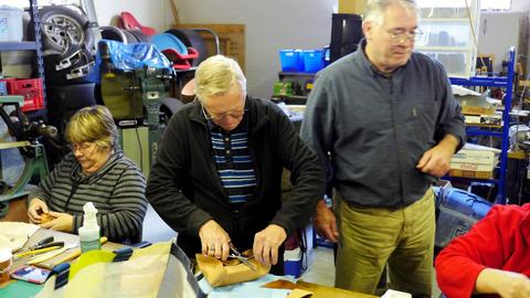 A man stretches leather over a form as a woman works beside him and another man watches