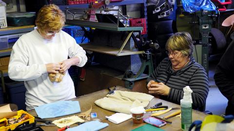 Two women shape damp leather around small box forms at a workshop table