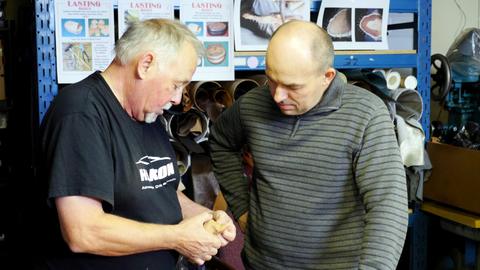 Two men look closely at a lasted leather box in progress in front of lasting box posters