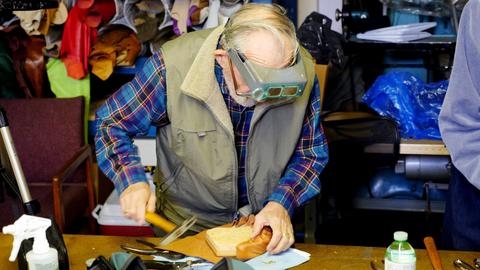 A man in a headband magnifier hammers tacks into leather lasted over a form