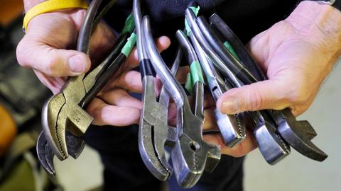 A hand holds a bundle of lasting pliers with green-taped handles