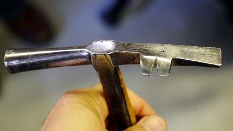 Close view of a hand holding a lasting hammer with a notched claw on its head
