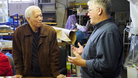Two men in conversation at the workshop, one gesturing as he explains