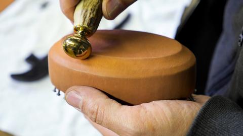 A bone folder-like tool presses and smooths tan leather lasted over an oval form