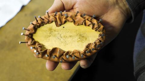 A hand holds an oval form with leather gathered and tacked all around its edge