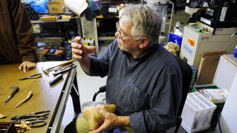 A seated man holds a box form, tools laid out along the bench beside him