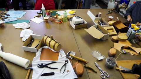 A cluttered workshop table with box forms, lasting pliers, scissors, tacks and leather scraps