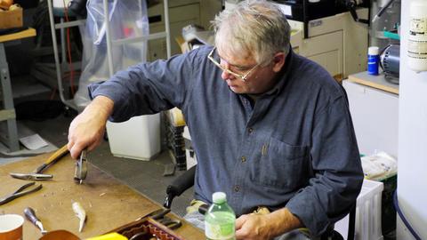 A man uses pliers at a workbench with knives and a water bottle near his hand