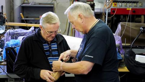 Two men work together pulling leather over a box form at the workshop