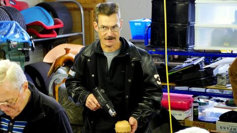 A man in a black leather jacket holds a heat gun over a leather-covered box form