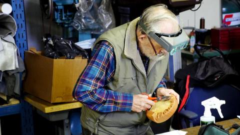 A man in a headband magnifier trims leather around an oval form