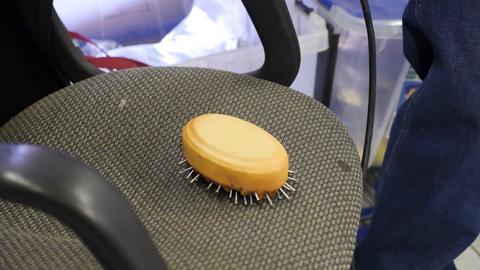 An oval form wrapped in tan leather and ringed with tacks sits on a mesh chair seat