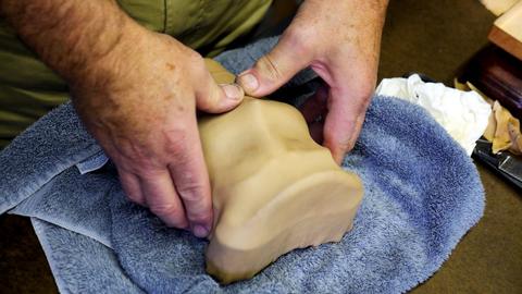 Hands press damp leather into the recesses of a shaped form on a towel