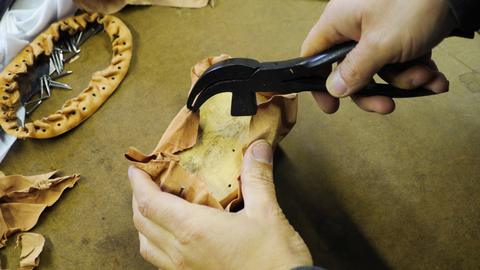 Lasting pliers pull tacks from leather moulded around an oval form