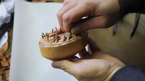 A hand presses tacks into leather on top of a round box form
