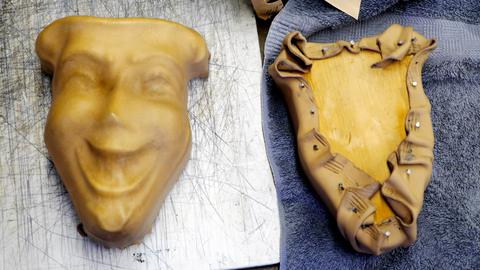 A leather mask moulded with a grinning face beside a form with leather gathered and tacked around it