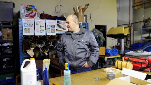 A man stands at a workshop table with glue, brushes and box forms in front of him