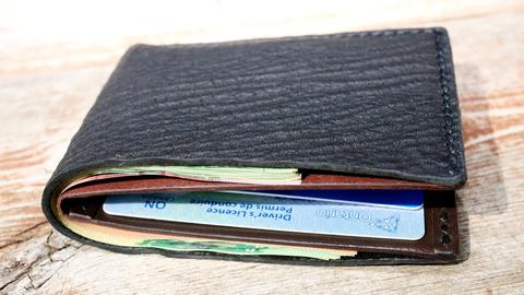 Black shark-leather bi-fold wallet, closed, with banknotes and cards inside