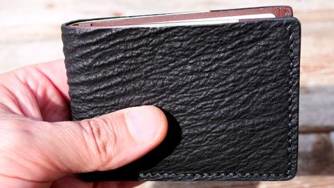 Black shark-leather bi-fold wallet held closed in the hand